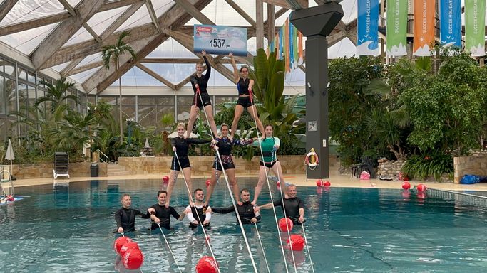 dreistöckige menschliche Pyramide im Schwimmbad, die oberen beiden Mädchen halten einen Scheck hoch